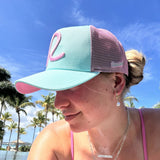 Woman wearing a pink and light blue cap with palm trees and blue sky in the background