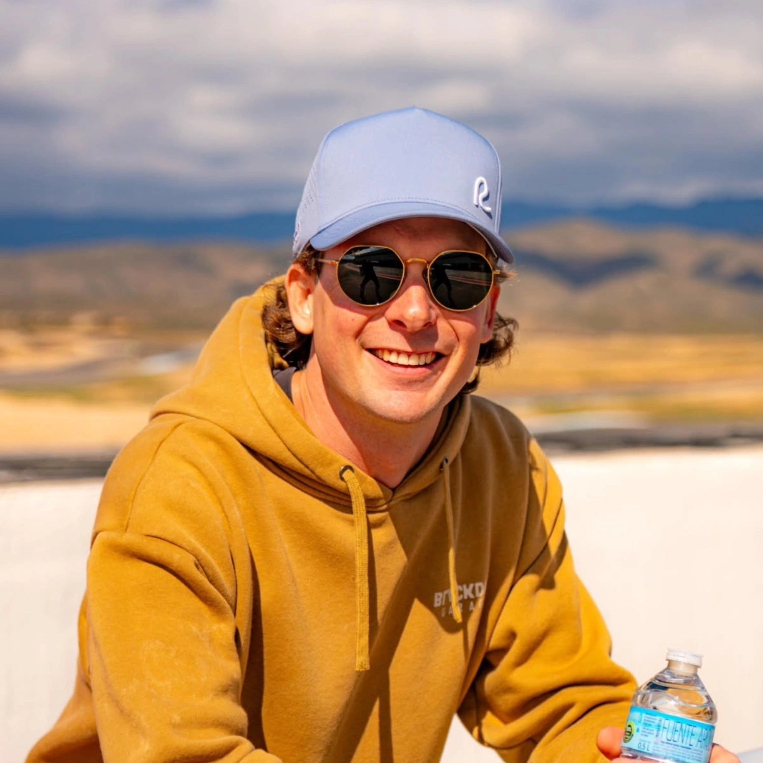 Person wearing a yellow hoodie and blue cap with sunglasses outdoors
